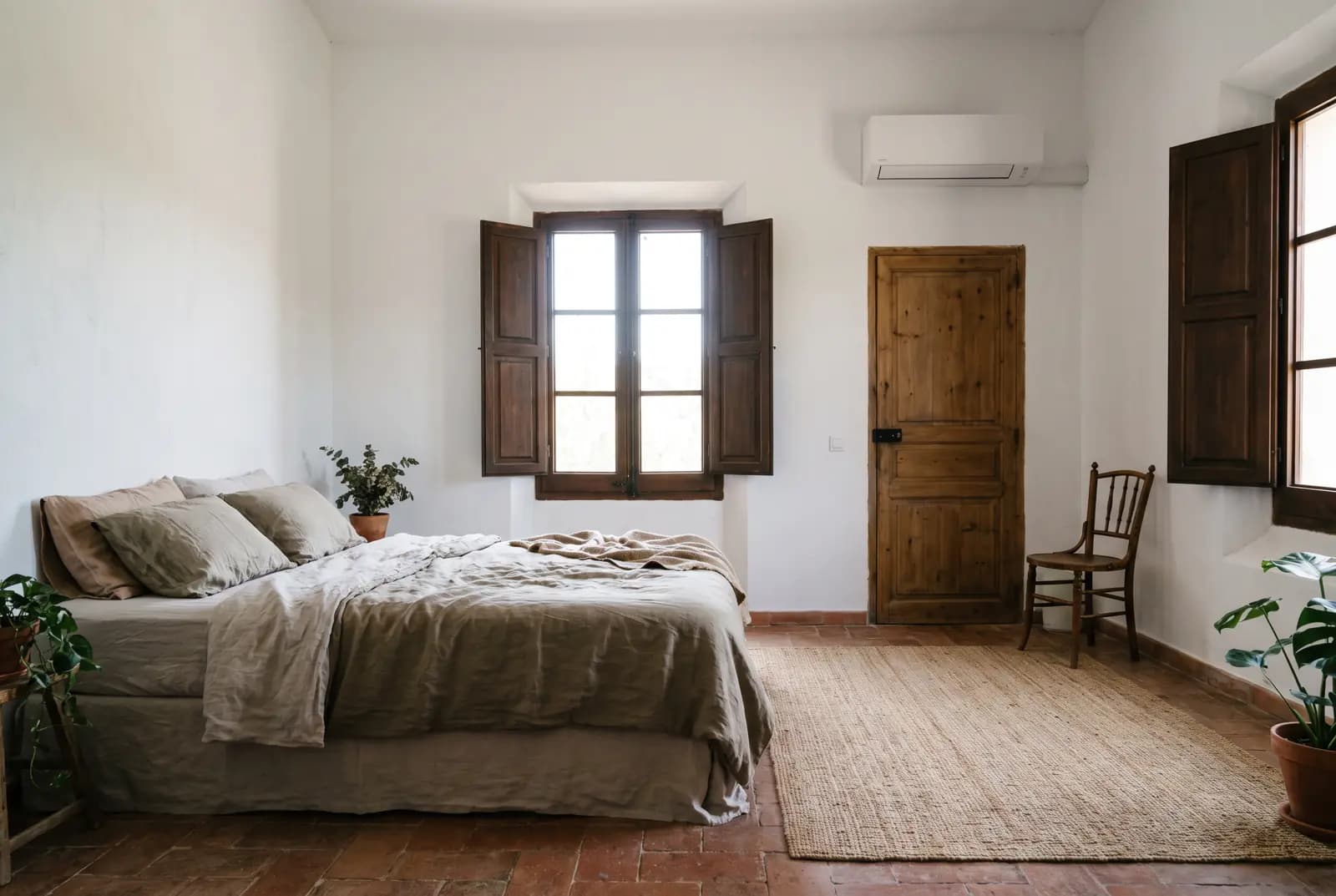 Chambre aux tomettes et volets bois, unité de climatisation murale au-dessus de la porte